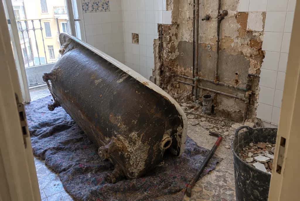 Bañera de hierro fundido retirada en un baño en obra, con las tuberías viejas a la vista