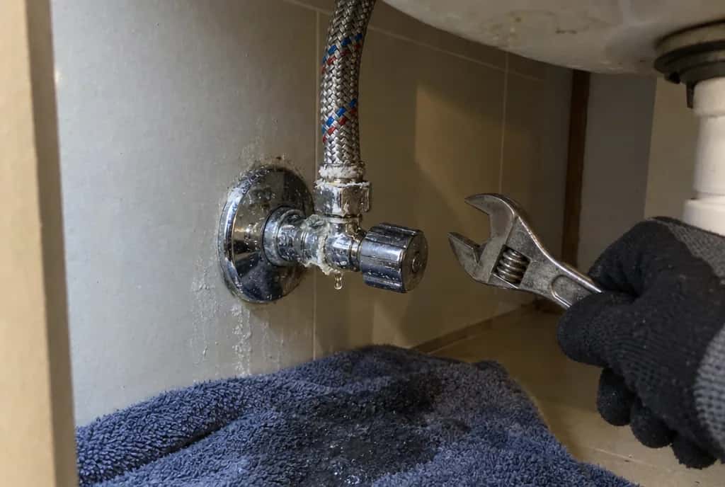 Llave de escuadra bajo un lavabo con una gota en la tuerca y cal alrededor