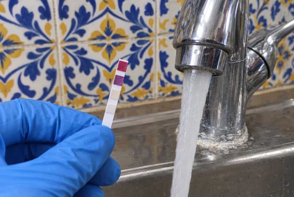 Tira de medición de la dureza del agua junto a un grifo abierto con cal en la base