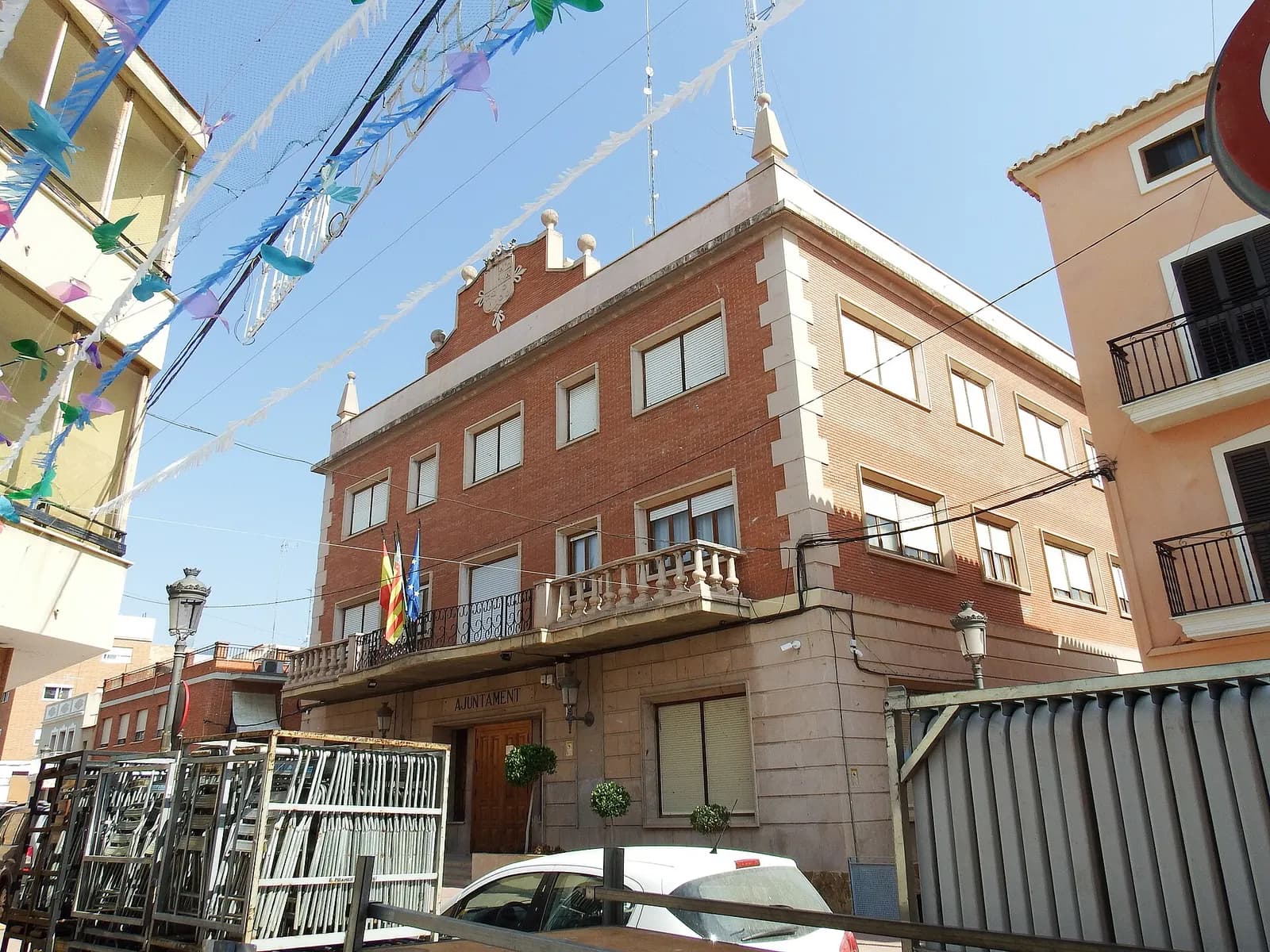 Ayuntamiento de Bétera, edificio de ladrillo con balcón y escudo, en una calle con adornos de fiestas