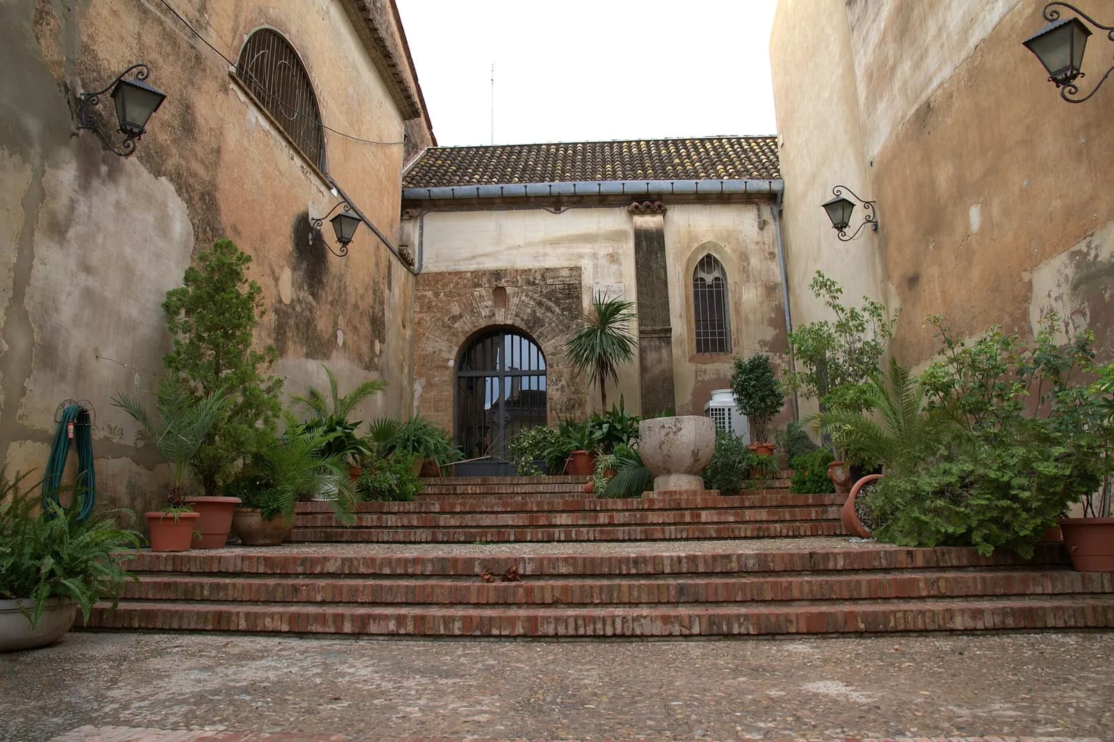 Escalinata con macetas junto a la iglesia parroquial de Godella, con muros antiguos y faroles
