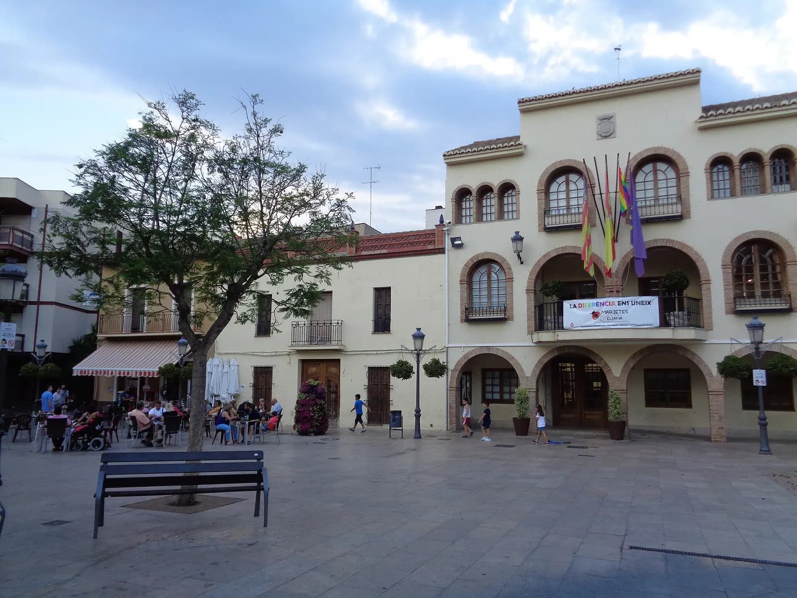 Ayuntamiento de l'Eliana con soportales de arcos y banderas, frente a una plaza con terrazas