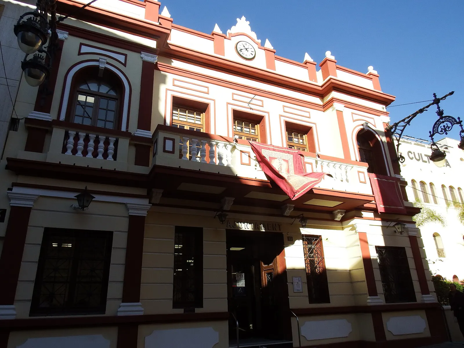 Fachada del Ayuntamiento de la Pobla de Vallbona, edificio de molduras rojas con reloj y balcón