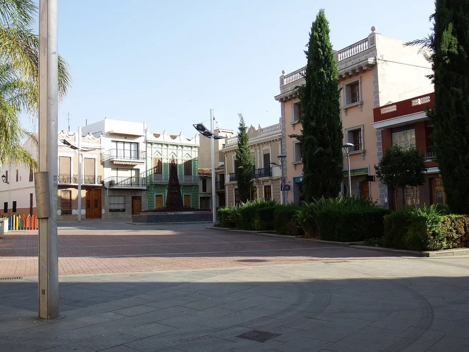 Plaza del centro de Picassent con cipreses y casas tradicionales de fachadas de colores al fondo