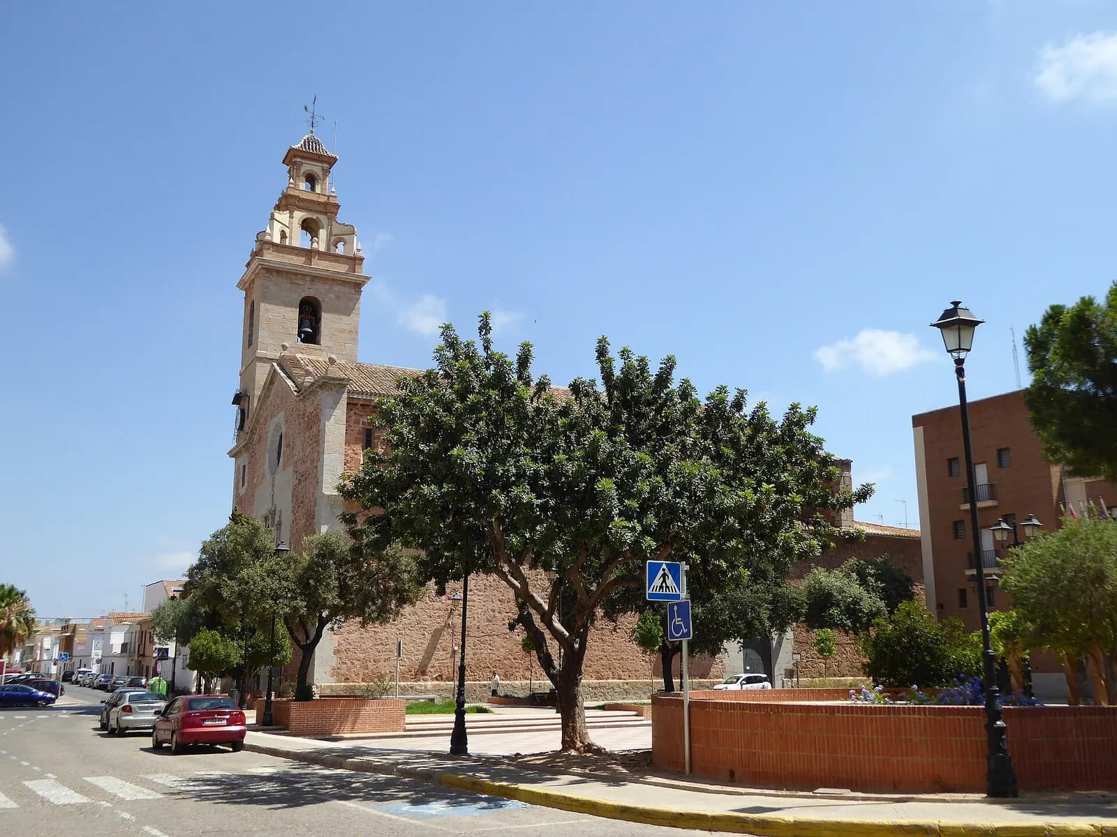 Iglesia de los Santos Juanes de Puçol, con su campanario, vista desde una calle con árboles y farolas