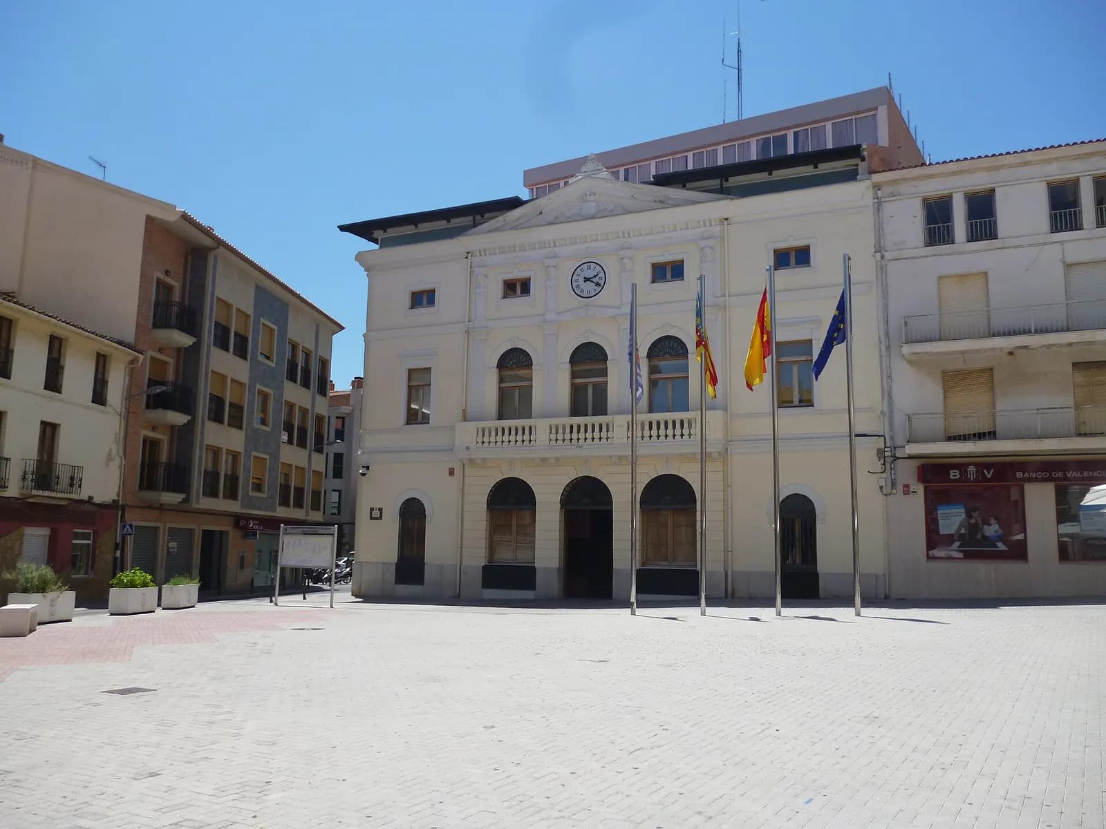 Ayuntamiento de Tavernes de la Valldigna con reloj, balcón corrido y banderas, frente a la plaza